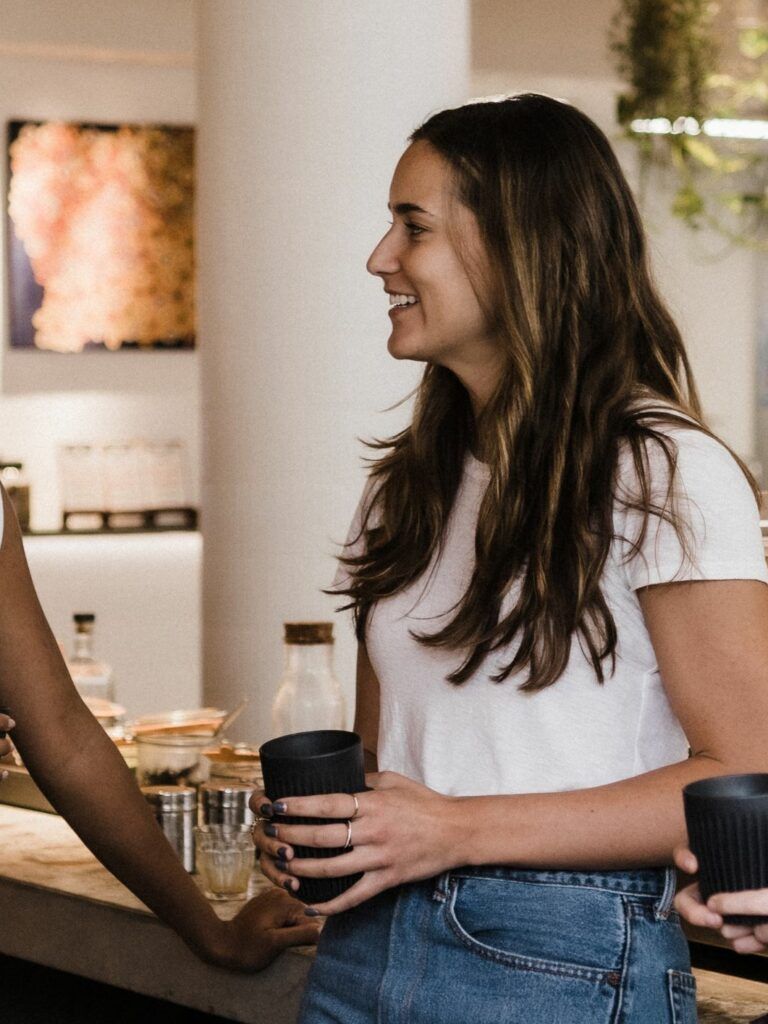 Tre personer i restaurangmiljö som samtalar medan de håller varsin svar kopp i händerna.